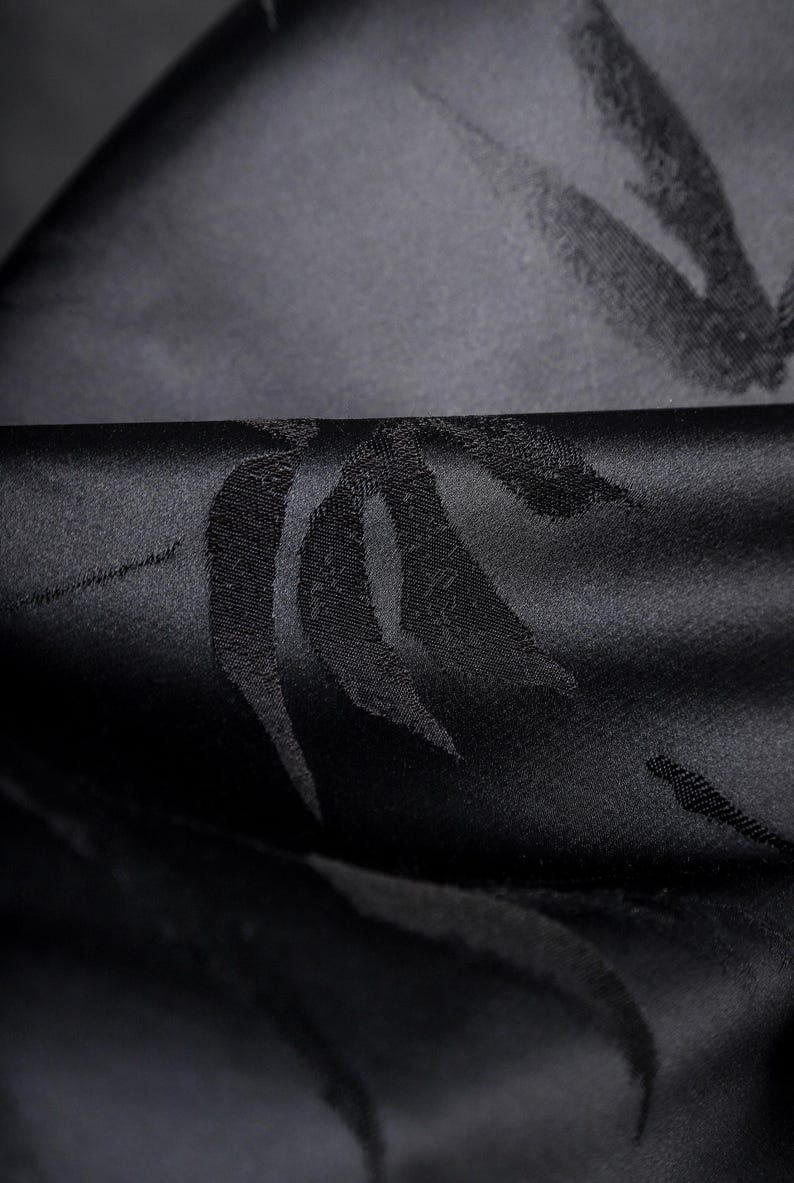 Puede incluir: Primer plano de tela negra con un patr&oacute;n sutil y repetitivo. La tela tiene una textura suave y satinada, con un ligero brillo. El patr&oacute;n parece ser un dise&ntilde;o estilizado de hoja o pluma.