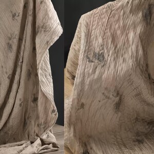 May include: A draped fabric in a neutral tone with a delicate floral pattern. The material has a textured, pleated look, with vertical lines and soft folds. The floral design is in muted shades, adding a gentle touch to the overall aesthetic.