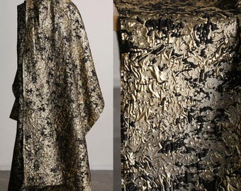 May include: A draped garment with a textured, metallic gold and black pattern. The fabric has a crinkled appearance, creating a dynamic visual effect. The overall aesthetic suggests a luxurious or high-fashion textile, suitable for apparel or decorative purposes.