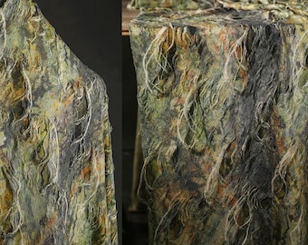 May include: Textured fabric with a camouflage pattern in shades of green, brown, and gray. The fabric has a rough, layered appearance with white, string-like details. The material is draped over a surface, suggesting its use in clothing or home decor.
