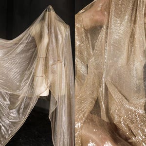 Puede incluir: Una tela brillante de color dorado drapeada sobre un maniquí. La tela tiene un tejido delicado en forma de red, que atrapa la luz y crea un efecto brillante. El material es fluido y parece ligero, adecuado para ropa de noche u ocasiones especiales.