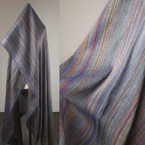 Könnte beinhalten: Ein drapierter Stoff mit vertikalen Streifen in Blau-, Lila-, Gold- und Rottönen. Der Stoff wird auf einer Schaufensterpuppe präsentiert, die seinen Fall und seine Textur zeigt. Die Nahaufnahme zeigt das komplizierte Gewebe und die Farbvariationen.