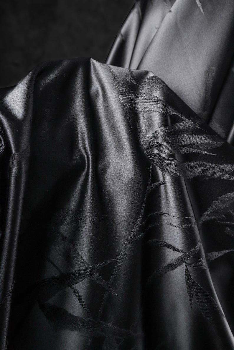 Puede incluir: Primer plano de tela negra con un brillo sutil. El material est&aacute; drapeado, revelando patrones intrincados y texturizados. El dise&ntilde;o presenta una serie de l&iacute;neas y formas que se cruzan, creando un efecto visual din&aacute;mico. El color oscuro y la textura de la tela sugieren lujo.