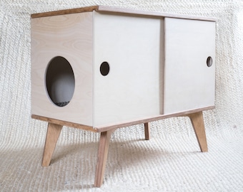 May include: A white wooden cat litter box with a sliding door and a round opening on the front. The box is on four wooden legs.