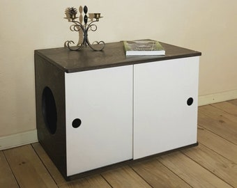 May include: A dark brown wooden cabinet with two white doors. The cabinet has a cutout for a litter box and a small decorative candle holder on top. The cabinet is sitting on a wooden floor.