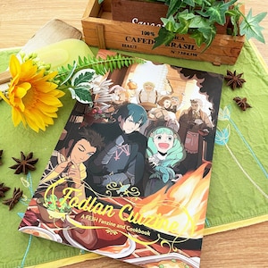 May include: A yellow and gold cookbook with the title "Fodlan Cuisine: A FE3H Fanzine and Cookbook" on the cover. The cover features a group of anime characters in front of a fire.