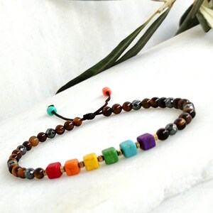 Peut inclure: Un bracelet arc-en-ciel avec des perles brunes et noires. Le bracelet a une fermeture à nœud coulissant.