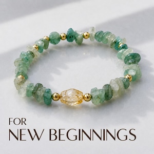 May include: A stretch bracelet featuring irregular, tumbled green gemstone chips interspersed with small, polished gold-tone metal beads. A single, faceted, translucent yellow-orange gemstone bead is centred. The text FOR NEW BEGINNINGS is below.