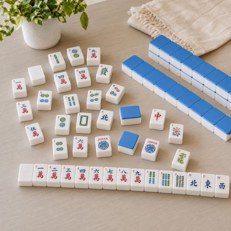 May include: A set of white Mahjong tiles featuring various Chinese characters, numbers, and symbols in red, blue, and green ink. Some tiles have blue backs, while others display specific game icons like Joker, flowers, and directional markers.