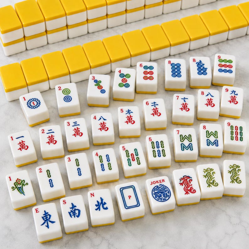 May include: A set of white mahjong tiles with yellow backs, featuring various colourful engraved symbols, Chinese characters, numbers, and a Joker tile. The tiles are arranged in rows and scattered patterns, displaying intricate red, blue, and green designs.