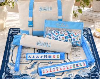 Puede incluir: Un juego de Mahjong que incluye un bolso de lona color crema y azul claro con el texto MAHJ, una bolsa transparente con cremallera etiquetada tiles, un estuche largo a juego, cuatro soportes azules translúcidos y una alfombrilla de juego.