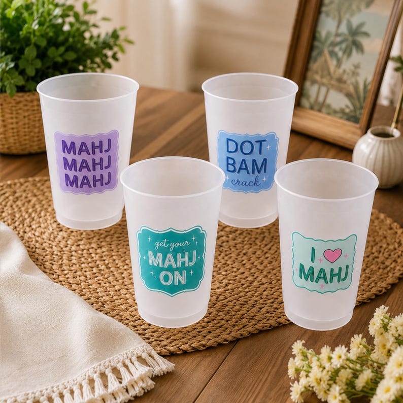 K&ouml;nnte beinhalten: Vier durchscheinende Kunststoffbecher mit bunten Etiketten und Text zum Thema Mahjong. Ein Becher zeigt MAHJ MAHJ MAHJ in Lila, einer DOT BAM crack in Blau, einer get your MAHJ ON in T&uuml;rkis und einer I heart MAHJ in T&uuml;rkis mit einem rosa Herz.