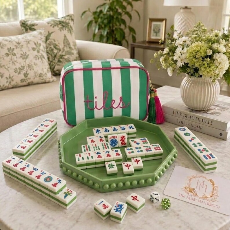 May include: A green and white striped zipped pouch with the word tiles embroidered in pink, a green octagonal tray, and a set of mahjong tiles with red, blue, and green characters. Two dice, a white card, and a stack of tiles are included.