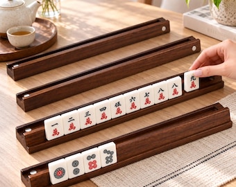 Könnte beinhalten: Ein Set aus dunkelbraunen Mahjong-Fliesenhaltern aus Holz mit einer Rille. Die Halter enthalten weiße, rechteckige Spielsteine mit roten und schwarzen chinesischen Schriftzeichen sowie kreisförmigen Mustern, angeordnet von eins bis neun.
