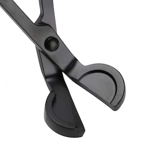 May include: Black metal candle wick trimmers with a scissor-like design. The trimmers have rounded edges and a black finish.