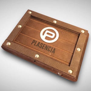 May include: A rectangular wooden box with a brown leather trim and silver studs. The box features the word "PLASENCIA" and a white logo on the wooden surface.