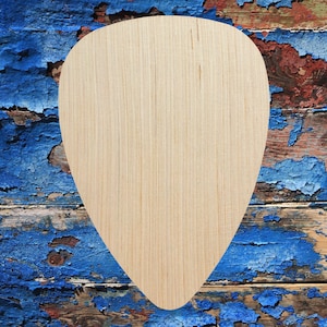 May include: A light-colored wooden guitar pick with a smooth surface. The pick is teardrop-shaped, with a rounded top and a pointed bottom. The background is a weathered wooden surface with peeling blue paint.