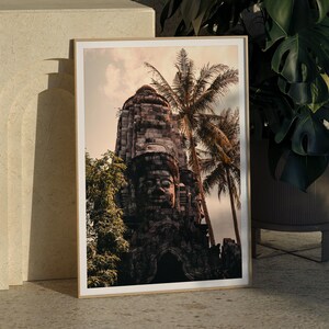 Puede incluir: Una fotografía enmarcada de un templo de piedra con una gran cara tallada. El templo está cubierto de exuberante vegetación verde y palmeras. La imagen tiene un ambiente cálido y vintage.