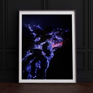 Pode incluir: Uma fotografia de perto de um fluxo de lava azul escuro e roxo com um toque de laranja no centro. A lava flui sobre uma superfície rochosa escura.