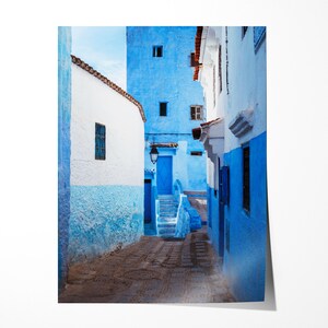 May include: A narrow, cobblestone alleyway in a Moroccan city, with white and blue painted buildings on either side. The buildings have arched doorways and windows, and the alleyway is lit by a single lamppost.
