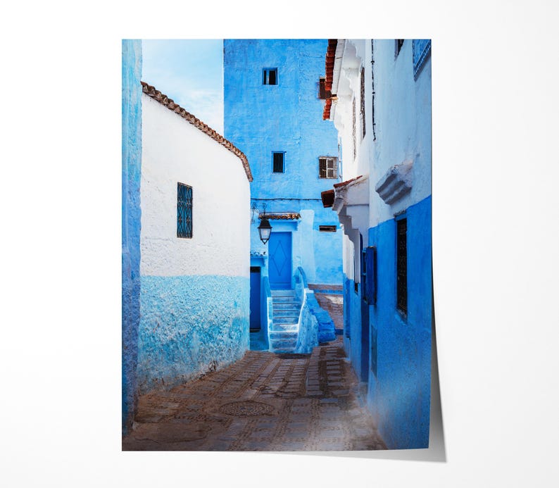 May include: A narrow, cobblestone alleyway in a Moroccan city, with white and blue painted buildings on either side. The buildings have arched doorways and windows, and the alleyway is lit by a single lamppost.