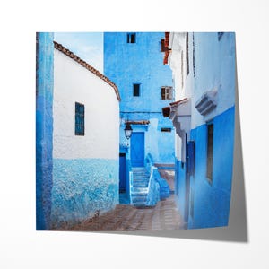 May include: A narrow, winding alleyway in a Moroccan city, with whitewashed walls and bright blue doors and windows. The walls are painted in a gradient of blue, fading from a deep blue at the top to a lighter blue at the bottom. The alleyway is lit by a single lamppost.