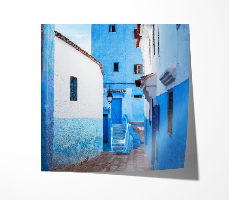 May include: A narrow, winding alleyway in a Moroccan city, with whitewashed walls and bright blue doors and windows. The walls are painted in a gradient of blue, fading from a deep blue at the top to a lighter blue at the bottom. The alleyway is lit by a single lamppost.