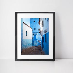 May include: A narrow, blue-painted alleyway in a Moroccan city. The walls are a vibrant shade of blue, and the steps leading up to the top of the alley are made of stone. The alley is lined with buildings on both sides, and the sky is visible at the top of the image.