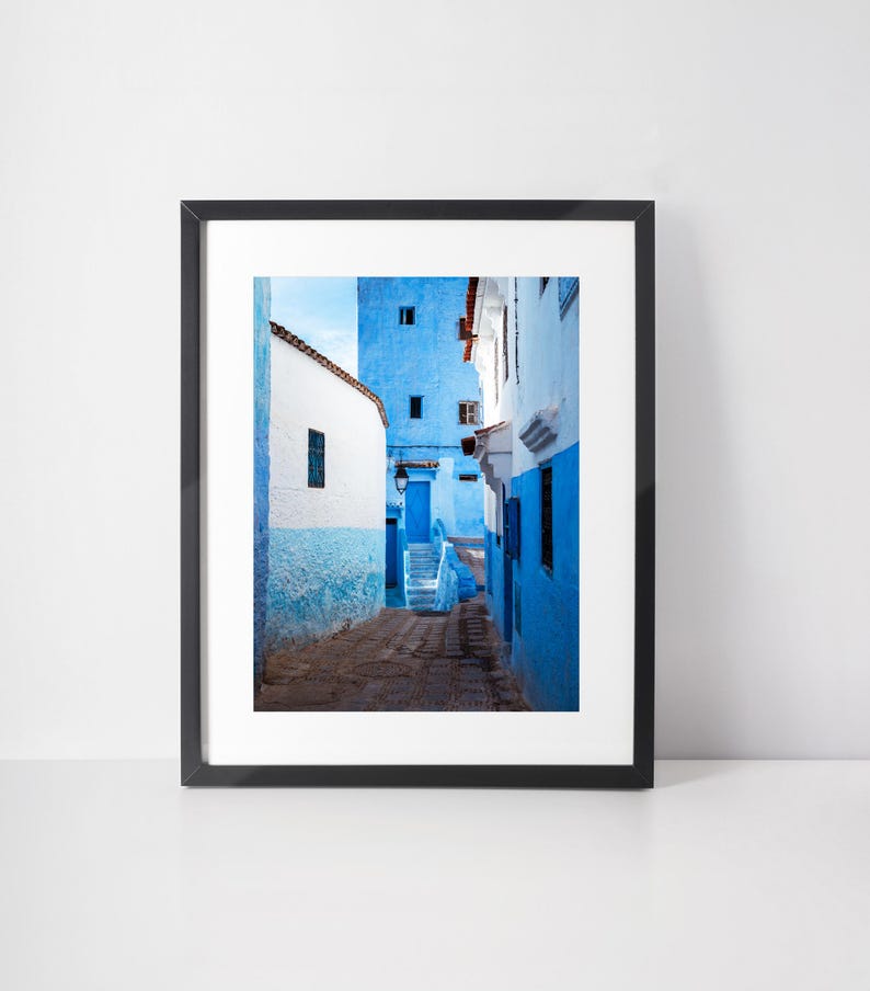 May include: A narrow, blue-painted alleyway in a Moroccan city. The walls are a vibrant shade of blue, and the steps leading up to the top of the alley are made of stone. The alley is lined with buildings on both sides, and the sky is visible at the top of the image.