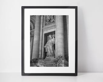 May include: Black and white photograph of a statue of a woman holding a staff, standing in a niche in a building with columns. The building is made of stone and has a weathered look. The text "FONTIBUS AGONIS MAGNI" is inscribed on the building.