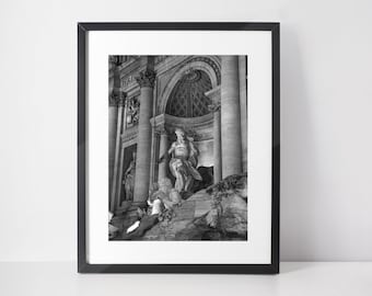 May include: Black and white photograph of the Trevi Fountain in Rome, Italy. The fountain is a large, ornate structure with a statue of Oceanus in the center. The fountain is surrounded by columns and arches.