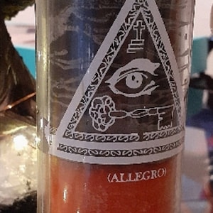 May include: A 7 Day Candle with a red wax base and a white label that says "DOUBL ACTION CANDLE (ALLEGRO)". The label also features a black and white image of an eye inside a triangle.