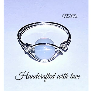 May include: A silver ring with a white opal stone. The ring is handcrafted and has the text "Handcrafted with love" written below it.