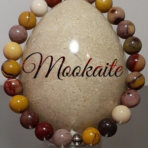 May include: A multi-colored beaded bracelet made of Mookaite stones. The bracelet features a mix of red, brown, yellow, and white stones.