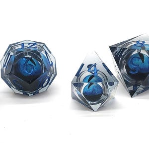 May include: Set of seven polyhedral dice with a blue and white design encased in clear resin. The dice include a cube, a d20, a d12, a d10, a d8, and two d6s. Each die has a different geometric shape.