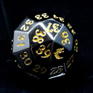 May include: A multi-faceted polyhedral die with a polished black metallic finish and engraved gold numbers. The die features numbers ranging from 26 to 39, with a small gold dragon icon replacing one of the numerical values on the top surface.