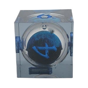 May include: A clear, cube-shaped art piece with a spherical interior. Inside the sphere is a dark blue design with a lighter blue symbol. The cube has blue accents and a reflective surface.