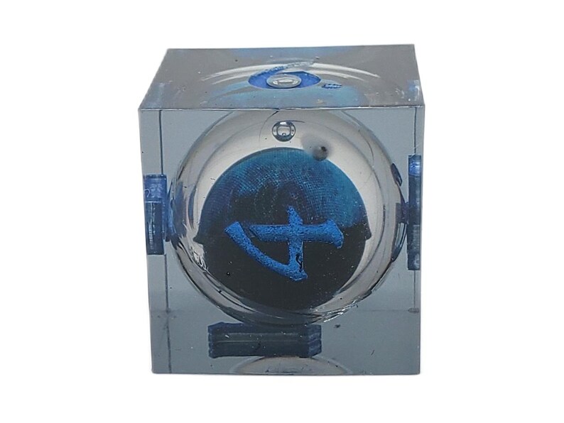 May include: A clear, cube-shaped art piece with a spherical interior. Inside the sphere is a dark blue design with a lighter blue symbol. The cube has blue accents and a reflective surface.