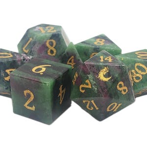 May include: Set of seven polyhedral dice in shades of green and burgundy, with gold numbering. The dice are made of a marbled stone-like material, suitable for tabletop role-playing games.