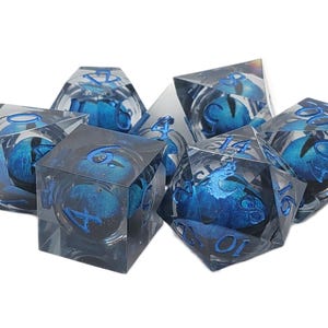 May include: Set of seven clear resin dice with blue and silver accents. Each die features blue internal designs and blue numbering. The dice are in various polyhedral shapes, including a cube, a d4, a d6, a d8, a d10, a d12, and a d20.