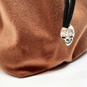 May include: A brown velvet dice bag with a silver skull charm. The bag has a drawstring closure and is perfect for storing dice.