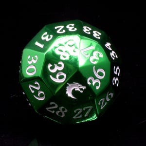 May include: A metallic green multi-sided die featuring white engraved numbers ranging from 26 to 39. The die has a polished finish and includes a small white graphic of a dragon head silhouette on one of its triangular faces among the numbers.
