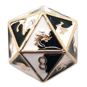 Puede incluir: Un dado de metal d20 negro y blanco con detalles dorados. El dado tiene un diseño de dragón en un lado y los números del 1 al 20 en los otros lados.