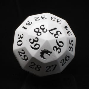 May include: A white multi-sided gaming die featuring black engraved numbers ranging from 26 to 39. The die has a distinct dragon icon printed in black on one of its triangular faces, positioned between the numbers 36 and 39 on the surface.