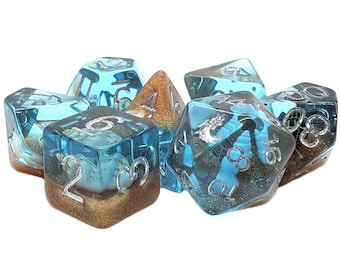 May include: Set of seven blue and gold dice with silver numbers. The dice are translucent and have a glittery finish. The dice are shaped like a cube, a pyramid, and a 20-sided die.