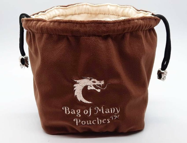 May include: A brown velvet dice bag with a white dragon design and the text "Bag of Many Pouches&trade;".