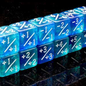 May include: A set of translucent blue and teal dice featuring white engraved mathematical symbols and numbers. Each face displays a fraction-like notation with positive or negative integers separated by a diagonal slash, arranged in a grid.