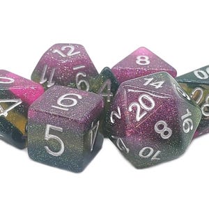 May include: Set of seven polyhedral dice in shades of purple, green, and gold with silver numbering. The dice are designed for tabletop role-playing games. The dice are made of a glittery resin material.