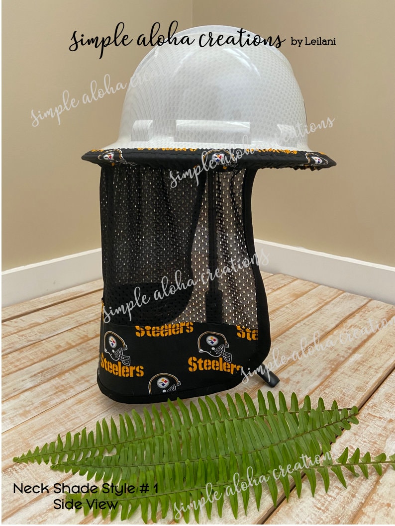 Pu&ograve; includere: Un casco bianco con un parasole in rete nera. Il parasole ha un motivo con il logo degli Steelers. Il casco &egrave; appoggiato su una superficie di legno con una pianta di felce verde in primo piano. Il testo "Neck Shade Style # 1 Side View" &egrave; visibile nell'immagine.