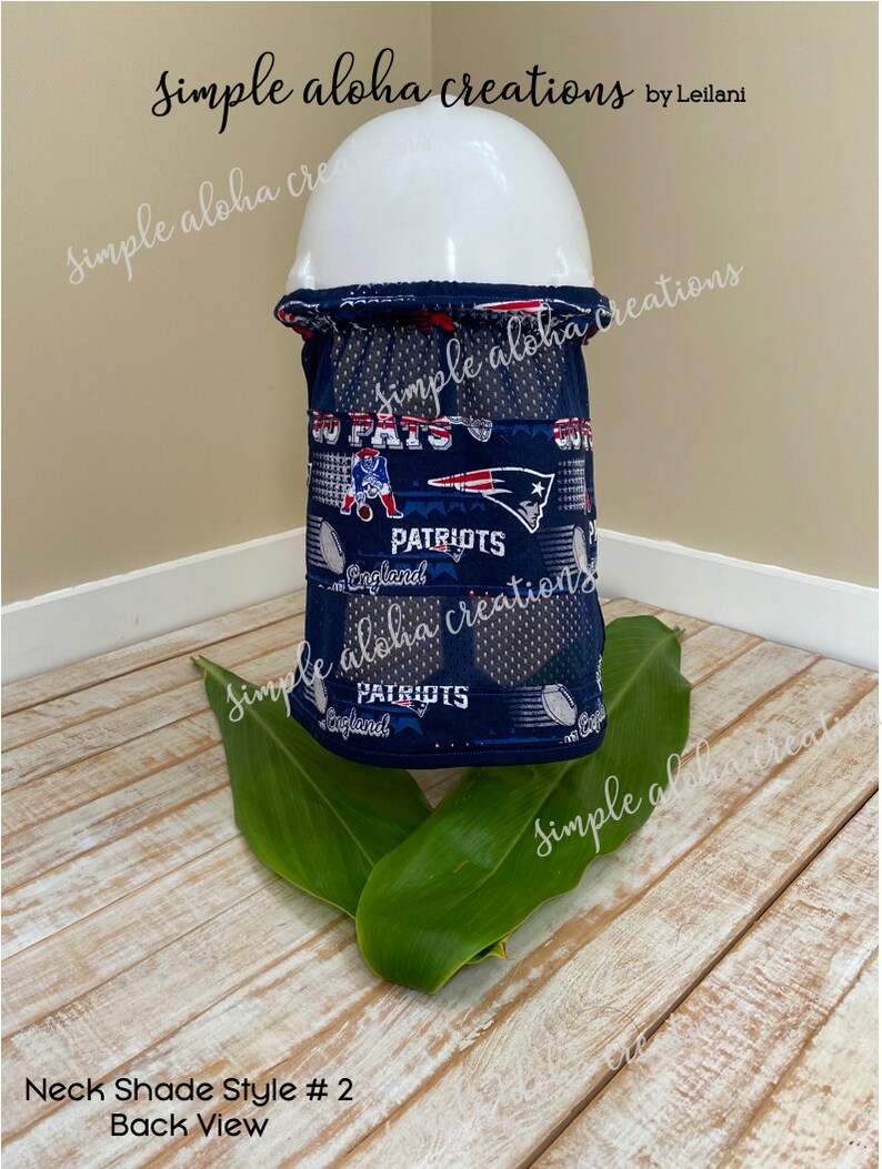 Pu&ograve; includere: Vista posteriore di un copricollo blu e bianco con un design dei New England Patriots. Il copricollo &egrave; realizzato in un tessuto traspirante e ha un pannello in rete per la ventilazione. Il testo "PATRIOTS" e "England" &egrave; visibile sul copricollo.